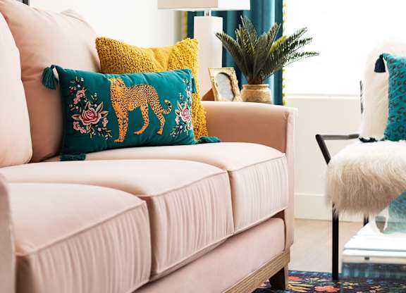A living room with a pink couch and a blue pillow.