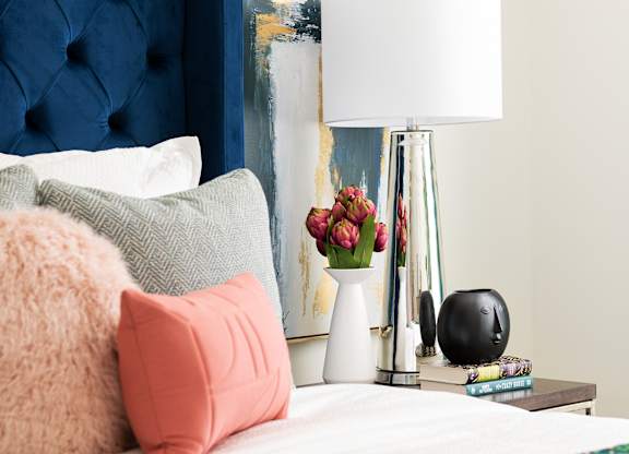 A bed with a blue headboard and a white lamp on a side table.
