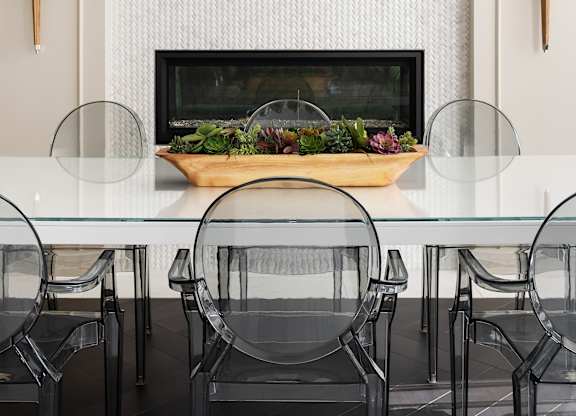A modern dining room with a glass table and black chairs.