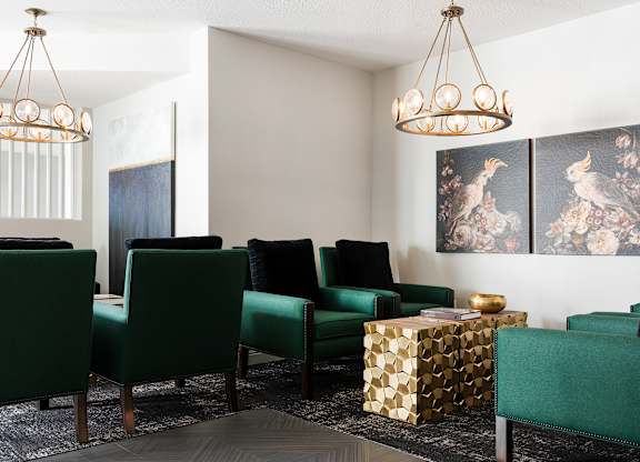 A living room with green chairs and a gold geometric ottoman.