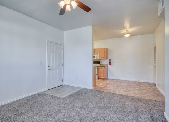 a living room with a ceiling fan and a kitchen in the background