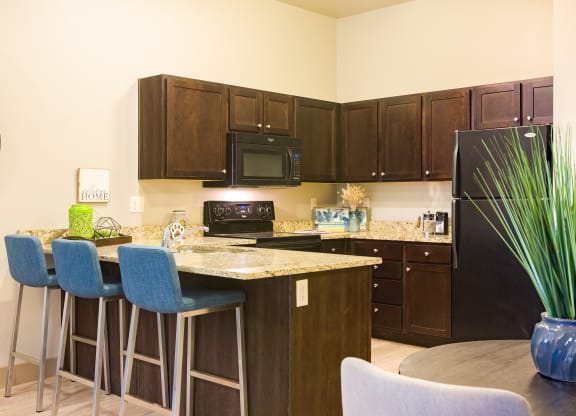a kitchen with an island with bar stools and a black refrigerator at Sugar House Apartments By Urbana, Salt Lake City, UT, 84105