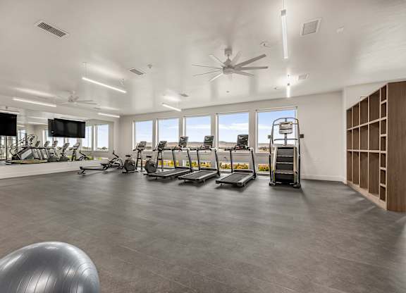 A spacious gym with treadmills, elliptical machines, and a fan.