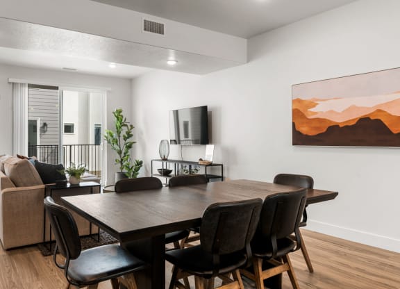 a dining room table with chairs and a couch in a room with white walls and hardwood