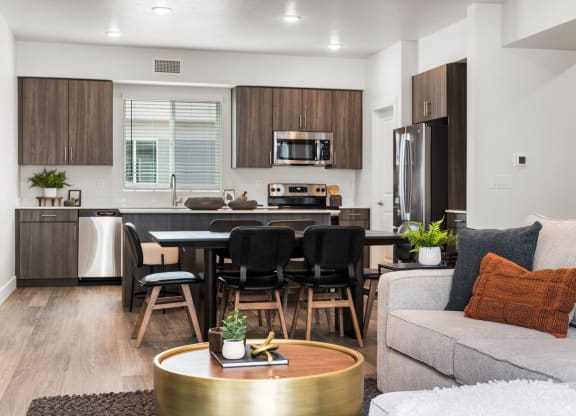 a living room with a couch a table and chairs and a kitchen with a refrigerator and microwave