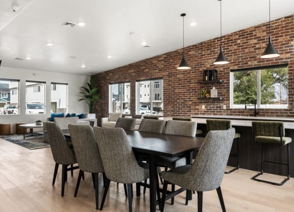 a dining area with a long table and chairs and a brick wall with windows in the background
