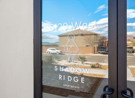 a window with a reflection of a building with a shadow ride sign on it