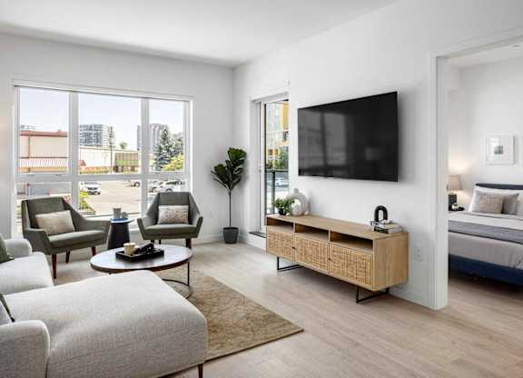 A modern living room with a large window, a sofa, a coffee table, a TV, and a bed.