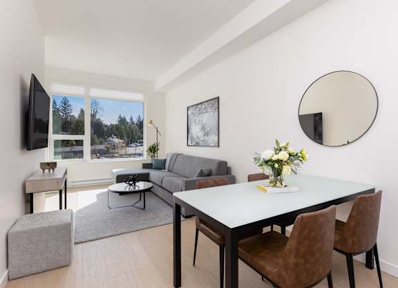 A modern living room with a grey sofa, a white dining table, and a television.