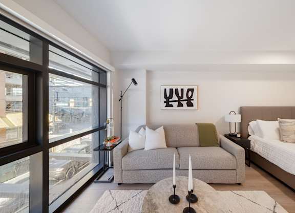 A modern living room with a large window and a grey sofa.