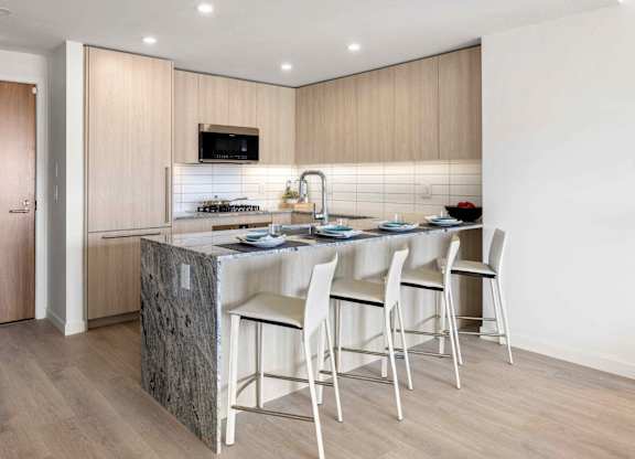 A kitchen with a granite island and white chairs.
