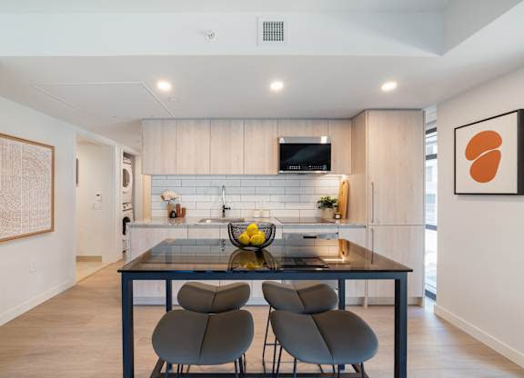 A modern kitchen with a glass table and grey chairs.