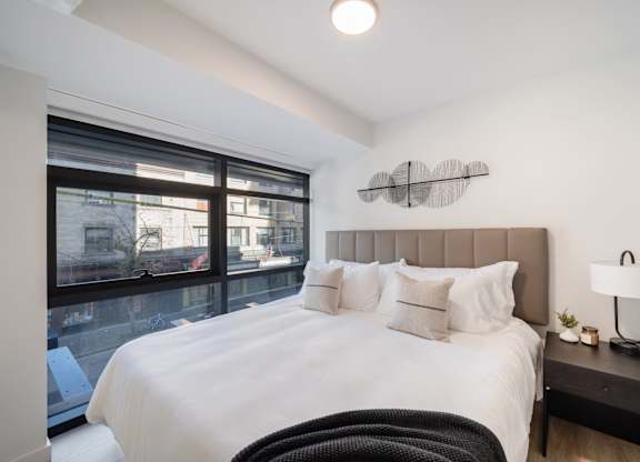 A bedroom with a large bed and a window overlooking a cityscape.