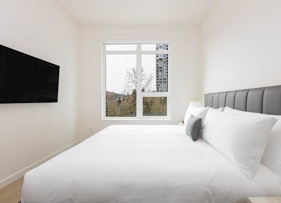 A white bed with a grey headboard and two pillows in a room with a window.