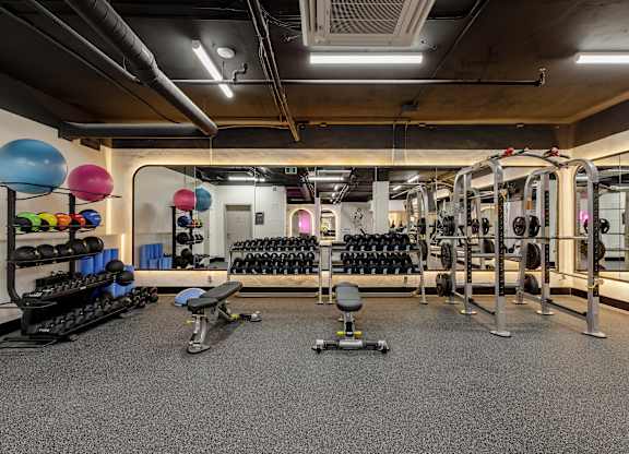A gym with a variety of equipment including dumbbells, weight plates, and a bench.