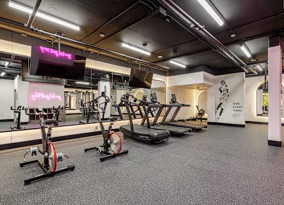 A gym with a row of stationary bikes and a television.