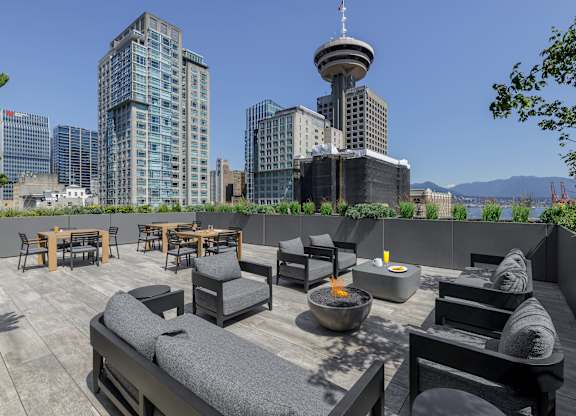 A rooftop patio with a fire pit and seating area overlooking a city skyline.