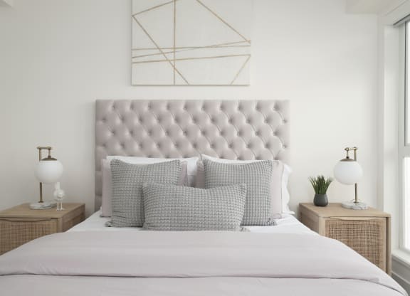a white bedroom with a bed with pillows and a geometric painting on the wall