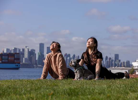 Two people sitting on the grass with a city skyline in the background.