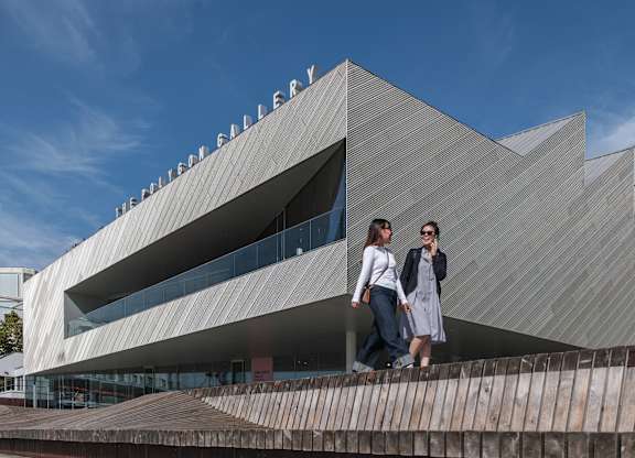 Two people are standing in front of a modern building with a unique triangular design.