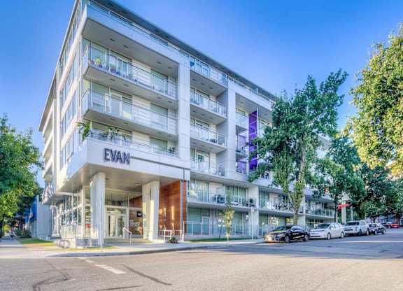 The image shows a modern apartment building named EVAN with cars parked in front and trees beside it.