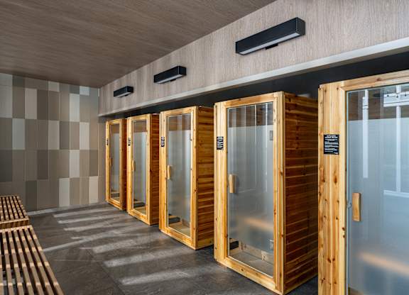 A row of wooden saunas with glass doors are lined up in a room.