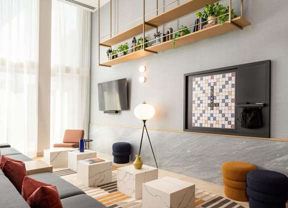 A modern living room with a grey sofa, a wooden shelf with plants, and a black and white tiled wall.