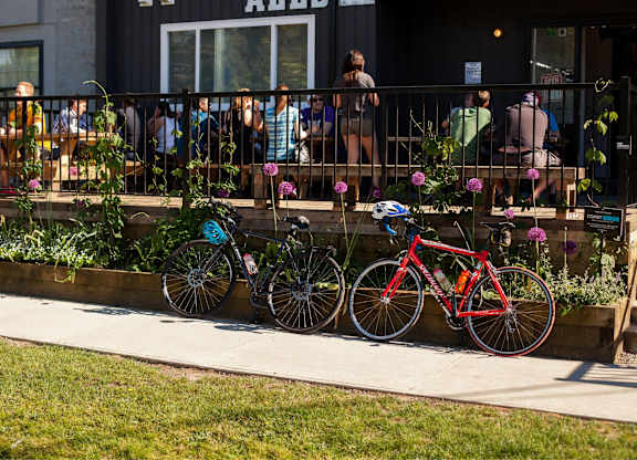 Two bikes are parked on a sidewalk next to a flower bed.
