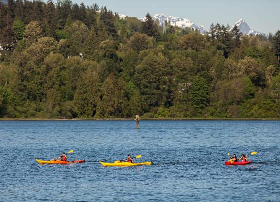 A group of people kayaking on a lake with a forested mountain in the background.