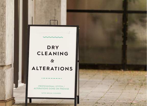 A sign that says dry cleaning and alterations is propped up against a wall.