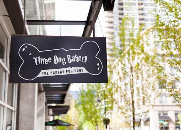 A black and white sign for Three Dog Bakery hangs from a building.