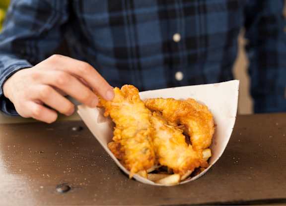 A person in a plaid shirt is holding a paper cone filled with fried food.