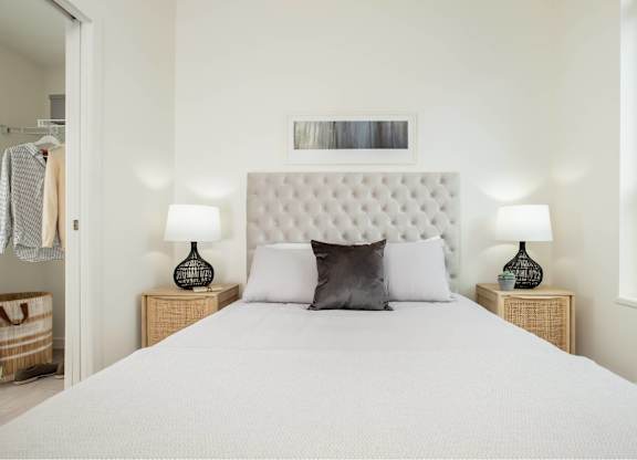 A bed with a white headboard and two pillows sits in a room with two lamps on either side.