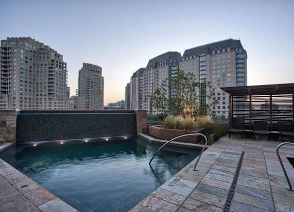 A pool area with a hot tub and a chair in front of a building.