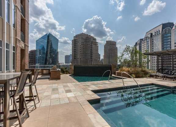 A swimming pool with a chair and a table is in the foreground with buildings in the background.