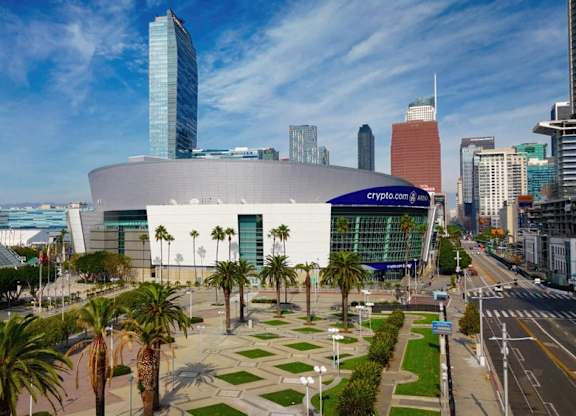 A modern building with a glass facade is surrounded by palm trees and other greenery.