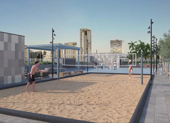 A man is playing beach volleyball in a sandy area with a city skyline in the background.