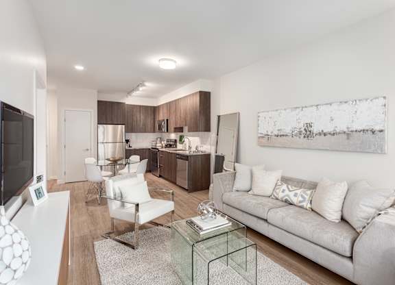 A modern living room with a grey couch, a glass coffee table, and a television.