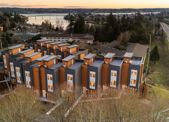 A large building complex with many windows is surrounded by a grassy area. at The Narrows at Clare Apartments , Washington, 98310