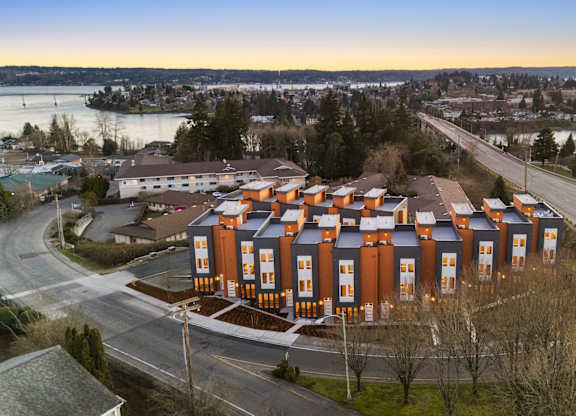 A large building with orange and blue exterior is surrounded by a road and trees. at The Narrows at Clare Apartments , Bremerton