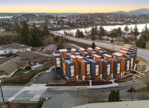 A large building with orange and white exterior is surrounded by a parking lot and other buildings. at The Narrows at Clare Apartments , Washington