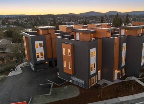 A modern building complex with orange and grey exterior is shown in the image. at The Narrows at Clare Apartments , Bremerton, 98310