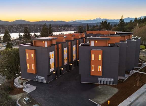 A modern building with orange windows is surrounded by a parking lot and trees. at The Narrows at Clare Apartments , Bremerton