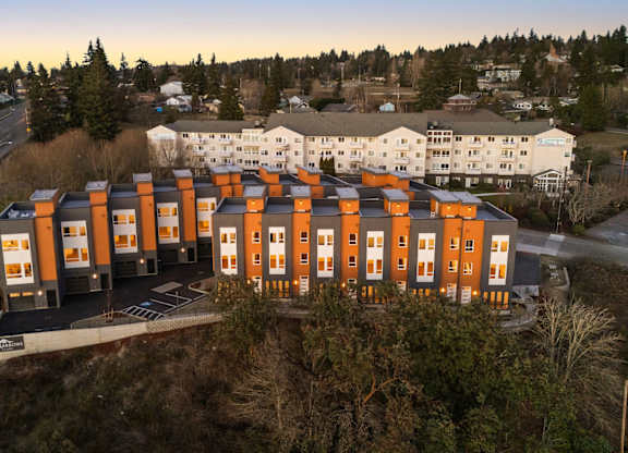 A large building with orange and white sections is surrounded by a parking lot. at The Narrows at Clare Apartments , Bremerton, WA, 98310