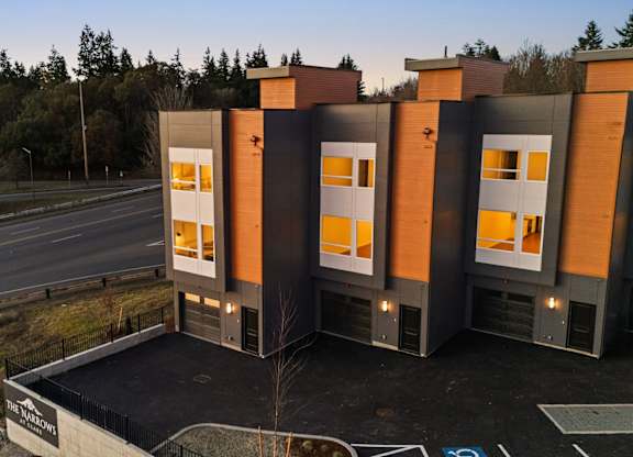 A modern building with orange and grey exterior is situated on a roadside. at The Narrows at Clare Apartments , Bremerton, Washington