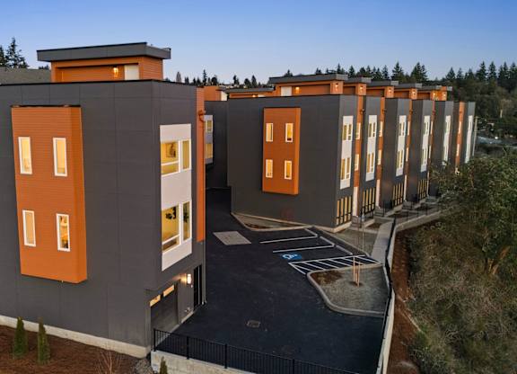 A modern building with orange accents and a parking lot in front. at The Narrows at Clare Apartments , Bremerton, WA, 98310