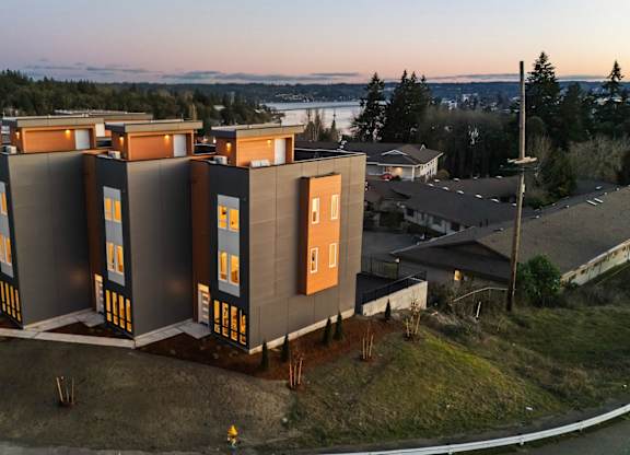 A series of modern buildings with orange doors are situated on a grassy area. at The Narrows at Clare Apartments , Bremerton