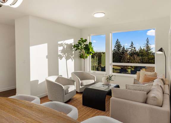 A living room with a large window, a grey sofa, a white armchair, a grey coffee table, and a potted plant. at The Narrows at Clare Apartments , Washington