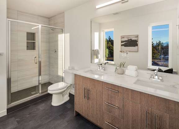 A bathroom with a walk-in shower, toilet, and double sinks. at The Narrows at Clare Apartments , Apartments, Bremerton, WA