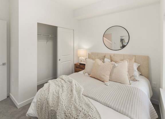 A bedroom with a bed, pillows, and a round mirror on the wall at The Narrows at Clare Apartments , Bremerton, 98310